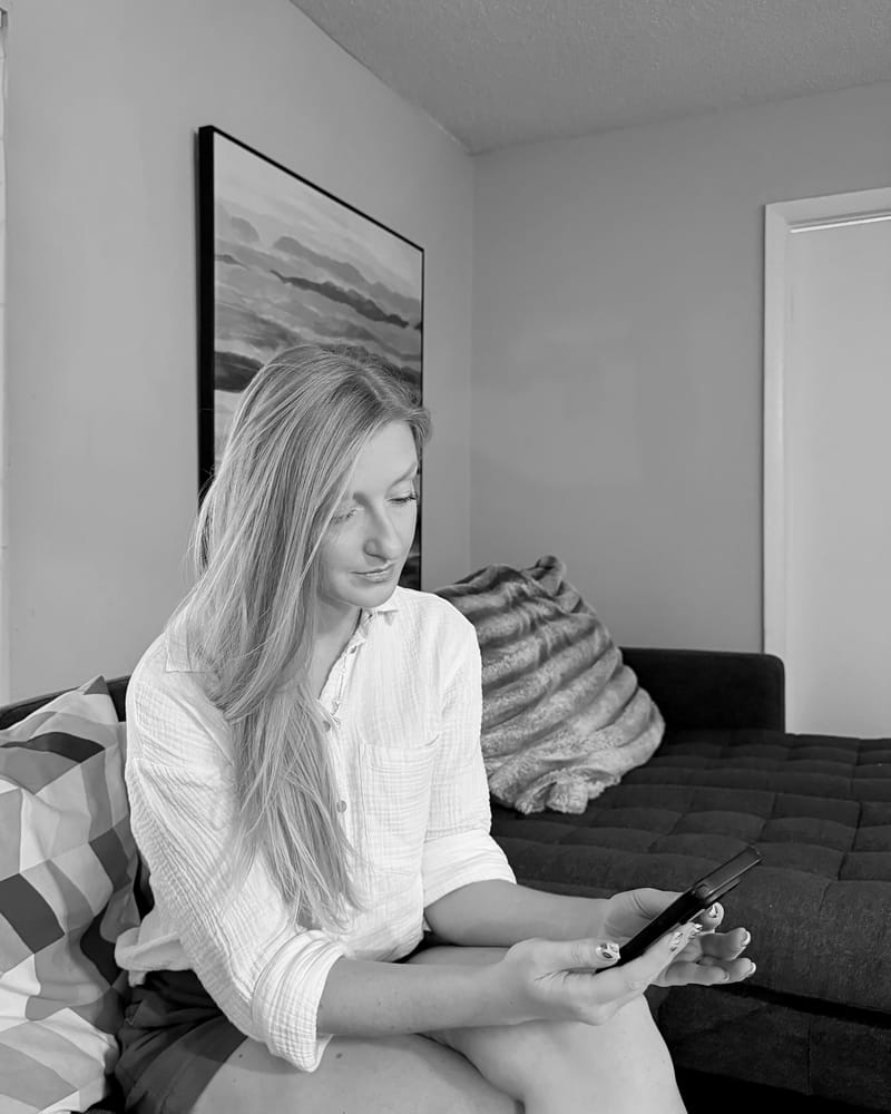 A woman on a sofa at home, looking calmly at her phone; black and white.